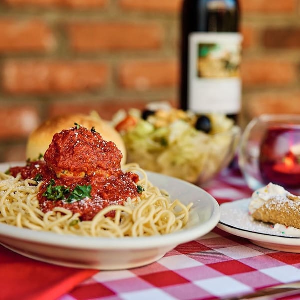 Miceli's spaghetti and meatballs, salad, bread, wine, and cannoli on a red and white checkered tablecloth.