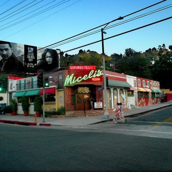 Exterior of Miceli's Pizzeria, a red brick building with green neon sign, on a sunny day.